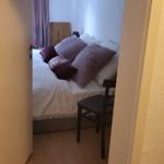 Schlafzimmer mit Bett, Kissen und Stuhl. Holzboden und Fenster mit Vorhängen.