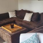Ein Wohnzimmer mit braunem Sofa, weißem Sessel und Wandbild eines Hochlandrindes.