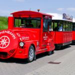 Roter Dünenschienenbus mit mehreren Wagen steht auf einem gepflasterten Weg.