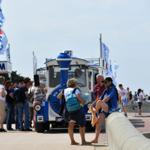 Besucher warten an einer Strandbahnstation. Ein blauer Zug steht bereit.
