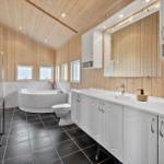 Bathroom with bathtub, toilet, and sink. Wooden walls and dark floor.