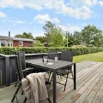 Deck with table and chairs, view of garden and hedge.