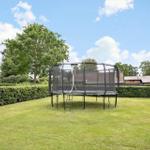 A black trampoline with net stands on a green lawn.