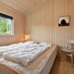Bedroom with wooden walls, bed, chair, and window with view of greenery.