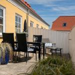 Terrasse mit Tisch, Stühlen und Pflanzen an gelbem Haus mit rotem Dach.