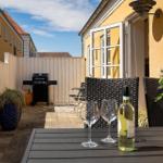 Terrasse mit Tisch, Stühlen, Grill und Blumen. Hinterhof mit gelbem Haus.