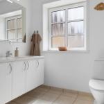 Badezimmer mit Waschbecken, Toilette und Fenster mit getöntem Glas.