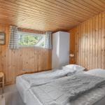 Schlafzimmer mit Holzwand, Bett, Kleiderschrank und Fenster mit Blick auf Wald.