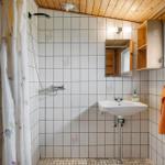 Badezimmer mit Dusche, Waschbecken und Holzregal an der Wand.