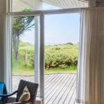 Durch große Fenster Blick auf eine Terrasse und Grünland bis zum Meer.