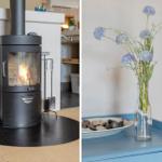 Kaminofen mit Holz und Blumen in Glasflasche auf blauem Tisch.