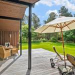 Deck with table, chairs, umbrella, and loungers before green lawn and forest.
