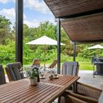 Terrace with dining table, chairs, umbrellas, and grill. View of green landscape.