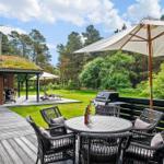 Deck with table, chairs, and umbrella. Grill and forest in background.