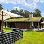 House with grass roof, terrace, sun loungers, and grill area in green surroundings.