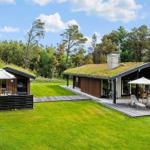 Two houses with grass roofs stand on green lawn. Terraces with umbrellas and lounge chairs.