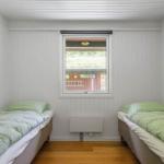 Two single beds with green bed linen are in a room with wooden floor and window.