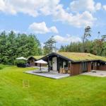 Modern wooden cabin with grass roof, terrace, and garden. Surrounded by trees under blue sky.