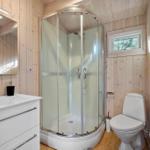 Badezimmer mit Dusche, Waschbecken und Toilette. Holzwände und Fenster.