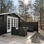 Schwarze Holzhütte mit Terrasse, Sitzgruppe und Feuerkorb im Wald.