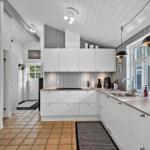 Moderne Küche mit weißen Schränken, Steinplatten und Fenster mit Blick nach draußen.