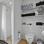 Badezimmer mit Dusche, Toilette und Regalen mit Handtüchern und Kosmetikartikeln.