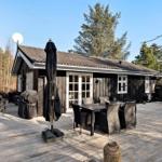 Holzhaus mit Terrasse, Tisch, Stühlen und Sonnenschirm. Umgeben von Bäumen und klarer Luft.