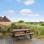 Holzterrasse mit Picknicktisch. Blick auf Grasland und ein rotes Haus mit Strohdach.