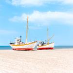 Zwei Fischerboote stehen auf dem Strand vor dem Meer unter blauem Himmel.