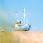 Ein blaues Fischerboot steht auf dem Strand, zwei kleinere Boote sind im Hintergrund zu sehen.