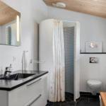 Badezimmer mit Dusche, Waschbecken und Toilette. Holzdecke und schwarzer Boden.
