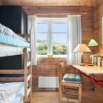 Zimmer mit Doppelstockbett, Schreibtisch und Fenster mit Blick auf Grün.