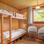 Zimmer mit Holzwand, Doppelstockbett und zwei weißen Stühlen neben Fenster.