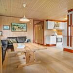 Wohn- und Küchenbereich mit Holzdecke, Sofa, Tisch und weißen Küchenmöbeln.