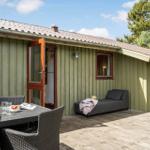 Terrasse mit Tisch, Stühlen und Liege. Hintergrund: Holzhaus mit offener Tür.