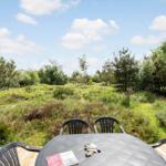 Rundtisch mit Stühlen auf Terrasse, Blick auf grüne Wiese und Bäume unter blauem Himmel.