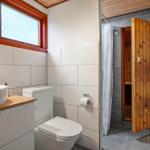 Badezimmer mit Waschbecken, Toilette und Dusche. Holzfenster und Sauna sind sichtbar.