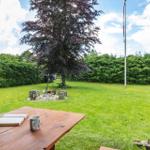 Von der Terrasse aus blickt man auf einen grünen Garten mit einem Baum und einem Grillplatz.