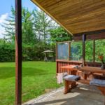 Holzterrasse mit Tisch und Bänken, Blick auf grünen Rasen und Wald.