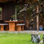 Holztisch mit Bänken auf Terrasse vor Holzhaus mit Blumen und Pflanzen.