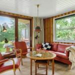 Ein Wohnzimmer mit roten Ledermöbeln, Holzwänden und großen Fenstern zum Garten.