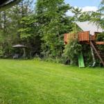Grüner Garten mit Baumhaus, Rutsche und Sonnenschirm.