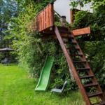 Holzhaus im Baum mit Leiter und grünem Rutschhang im Garten