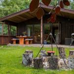 Holzhütte mit Grill, Tisch und Bänken im Garten. Rundum Grün und Bäume.