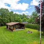 Holzhaus mit Terrasse, Grill und Feuerstelle auf grünem Grundstück umgeben von Bäumen.
