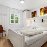 Ein Schlafzimmer mit weißem Bett, Holzboden und Fenster mit Blick auf Bäume.