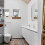 Badezimmer mit Toilette, Waschbecken und zwei Fenstern. Fliesenboden und Spiegelschrank.