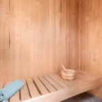 Sauna mit Holzwand, Bank, Holzschale und blauem Handtuch.