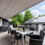 Terrasse mit Tisch, Stühlen und Grill unter Dach. Im Hintergrund Solaranlage auf Hausdach.