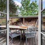 Terrasse mit Tisch und Stühlen, Holzstapel im Hintergrund, Blick in den Garten.